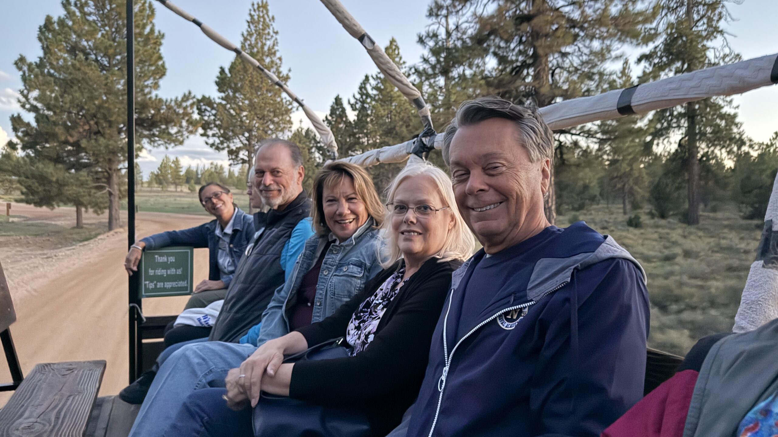 Friends smiling aboard the horse-drawn wagon on the way to the BBQ.